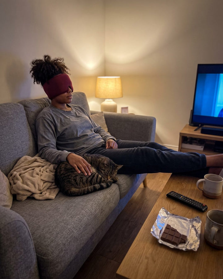 Frau sitzt mit der Kühlmaske auf dem Sofa, neben ihr eine Katze